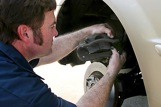 An auto mechanic working on disc brakes,  inserting new brake pads in the caliper.